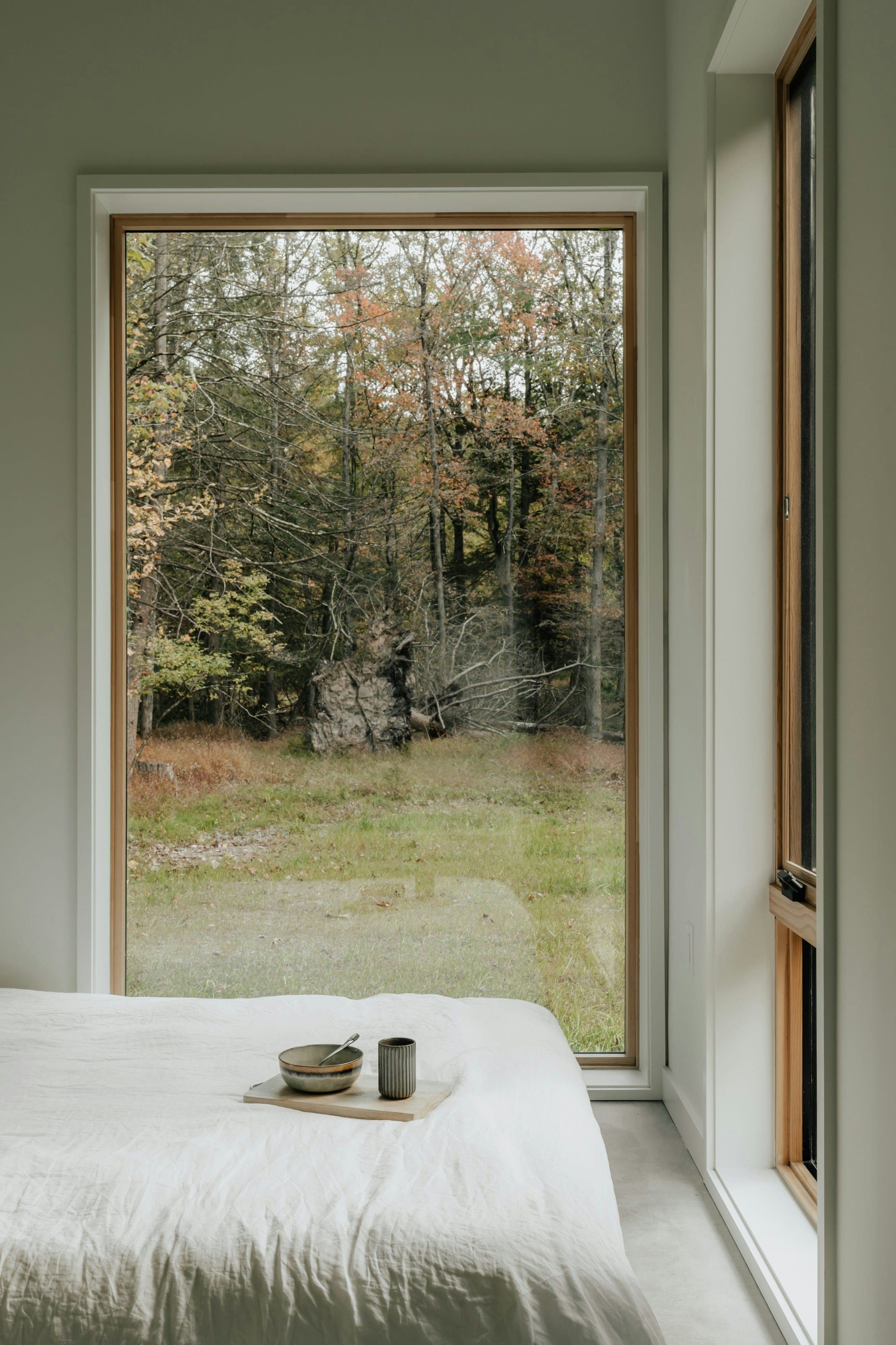 Chambre baignée de lumière avec grande fenêtre aluminium ouvrant sur la forêt — gamme SCELTA